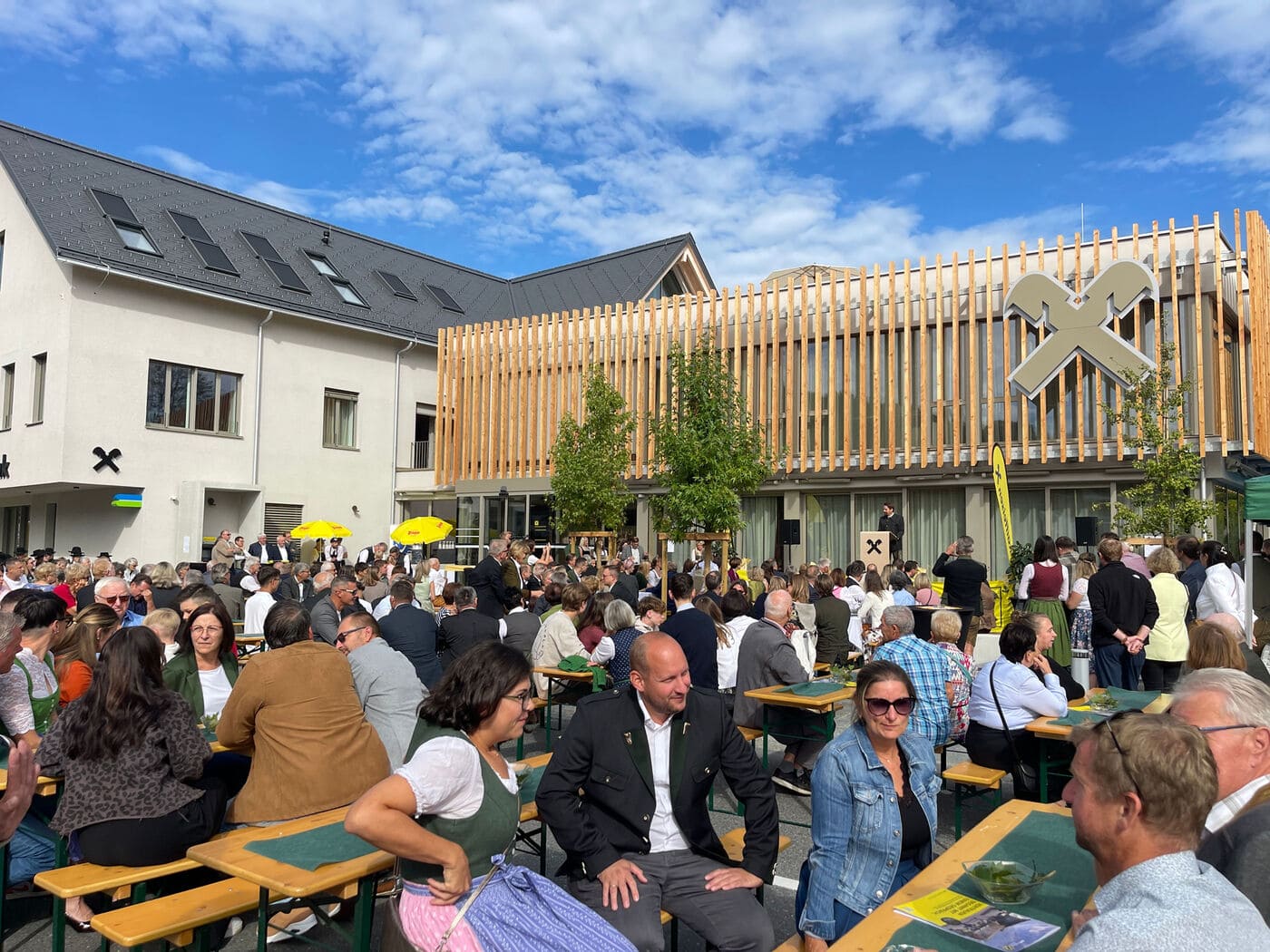 Festgäste auf dem Vorplatz der Raiffeisenbank Gamlitz vor dem sanierten Bestandsgebäude und dem Zubau mit Holzlamellenfassade