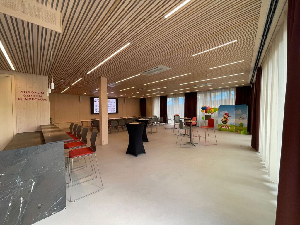 Veranstaltungssaal der Raiffeisenbank Gamlitz mit Holzlamellendecke, eingelassenen LED-Lichtlinien und Stehtischen